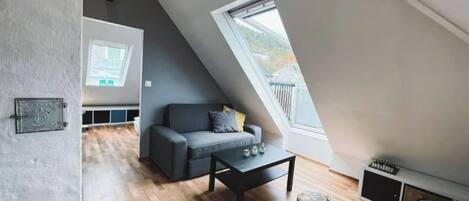 A modern loft with a sloped ceiling, a grey sofa, a coffee table, and a small ottoman.