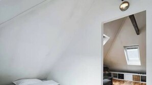 Une chambre avec un plancher en bois, un lit et une lucarne.