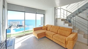 A modern living room with a large window, a corner sofa, and a staircase with glass railings. - Beautiful home in Cullera (Cullera)