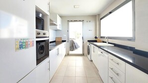 A narrow kitchen with a microwave, oven, and washing machine. There is a window providing natural light and a view of the outside. - Beautiful home in Cullera (Cullera)