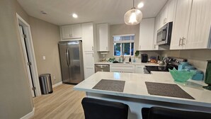 Een moderne keuken met witte kasten, roestvrijstalen apparatuur en een centraal eiland met barstoelen.