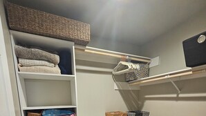 Een ruimtelijke opbergunit met planken en manden, een klein krukje en een pluizig vloerkleed op een houten vloer.