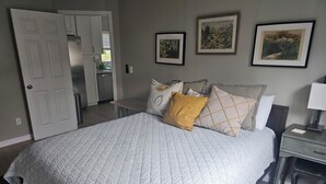 Een slaapkamer met een groot bed, een nachtkastje, een dressoir en een deur naar de badkamer.