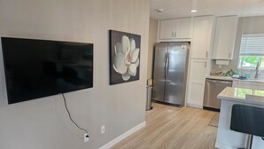 Een moderne keuken met witte kasten, een roestvrijstalen koelkast en een flatscreen televisie aan de wand bevestigd.