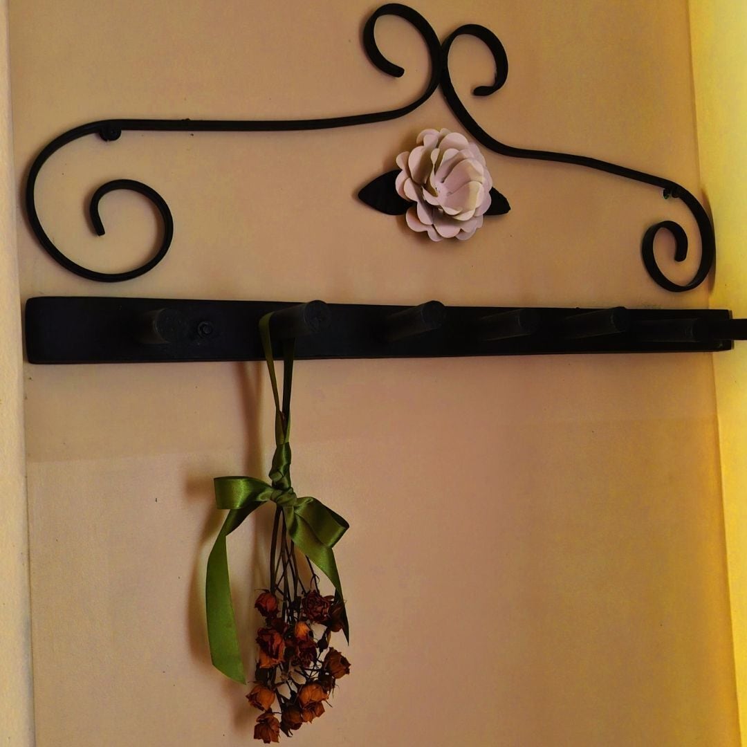 Un support métallique décoratif orné d’un motif floral et d’un ruban agrémenté de fleurs séchées.