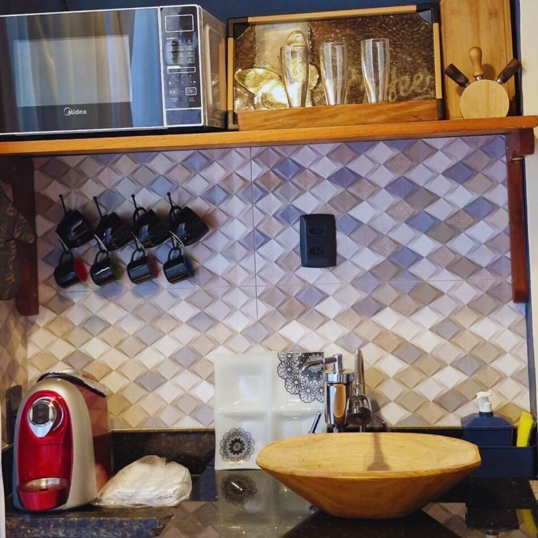 A kitchen with a microwave, a wooden shelf with glassware, a sink with a wooden basin, and a decorative backsplash.