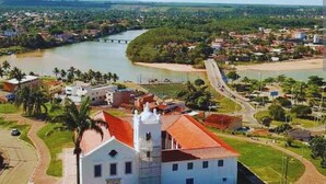 Un bâtiment blanc avec un toit rouge, probablement une église, entouré de verdure et bordé par une rivière.