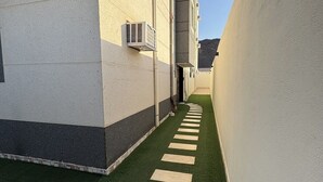 Un pasillo estrecho con suelo verde artificial y piedras beige para pisar.