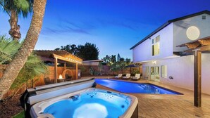 Un patio trasero con jacuzzi, piscina y zona de patio techada.