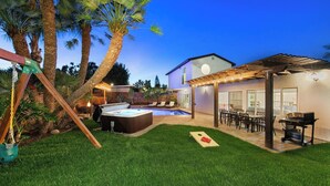 Un patio trasero con un jacuzzi, mobiliario exterior y una pérgola.