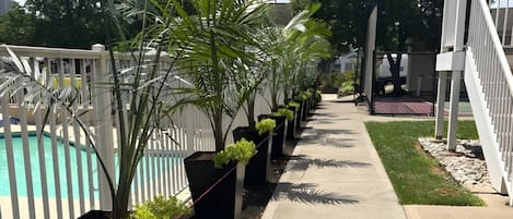 A poolside area with a white fence, potted plants, and a concrete walkway.