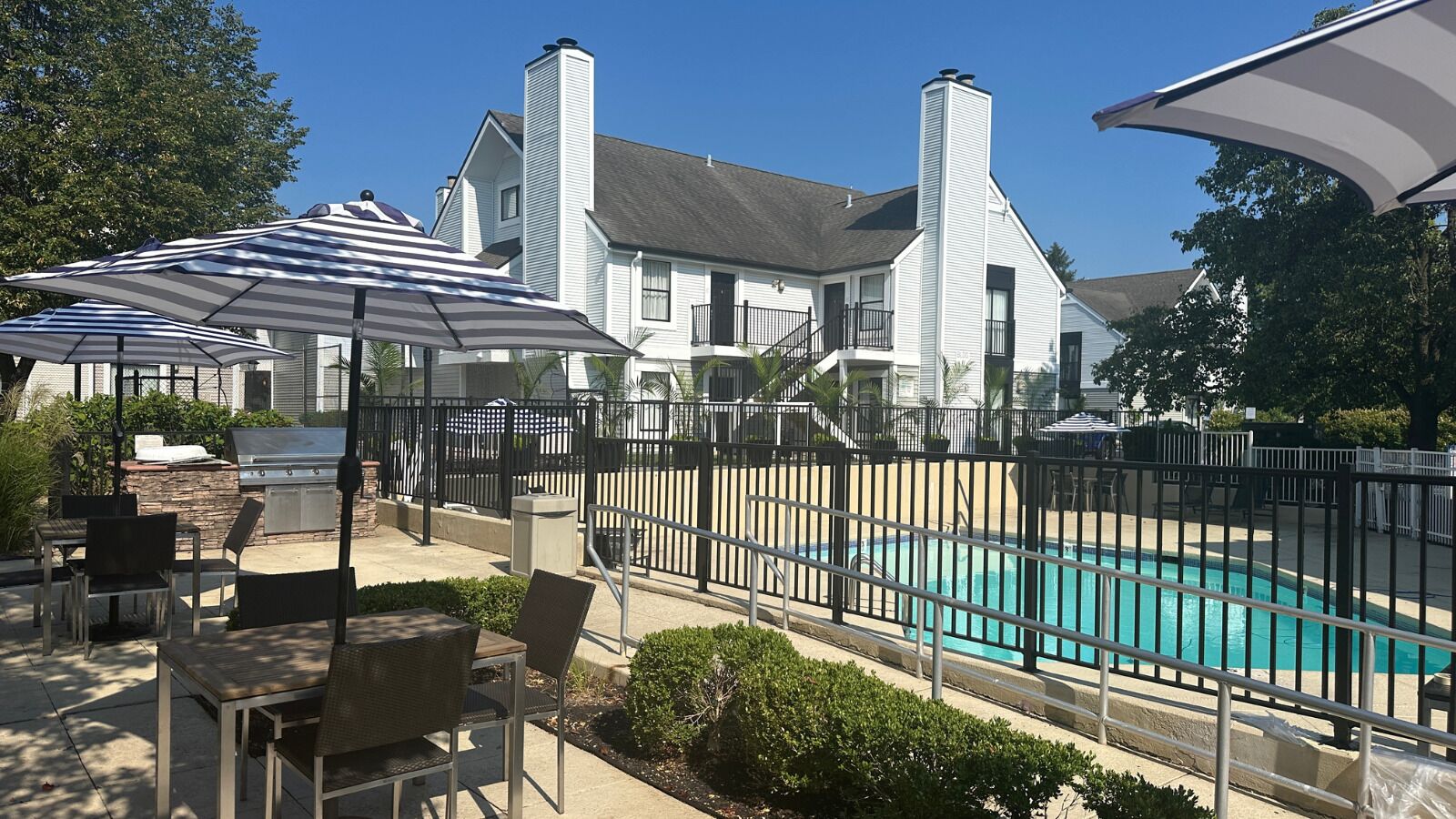 Un espace aménagé au bord de la piscine, avec une piscine entourée d’une clôture, des sièges d’extérieur et un barbecue.