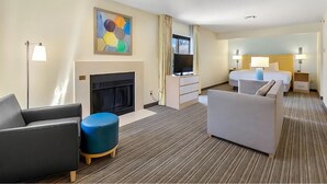 Quarto de hotel com lareira, televisão, cama e área de estar com um banquinho azul.