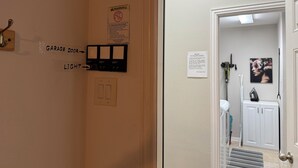 A hallway with a garage door, a light switch, and a warning sign. - Private Ground-Floor 2BR Suite in Gated Community - Near the Woodlands (Conroe)