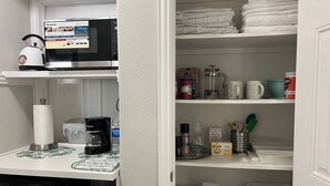 A kitchen with a microwave, coffee maker, and a tea kettle. There are shelves with folded towels and kitchen items. - Private Ground-Floor 2BR Suite in Gated Community - Near the Woodlands (Conroe)