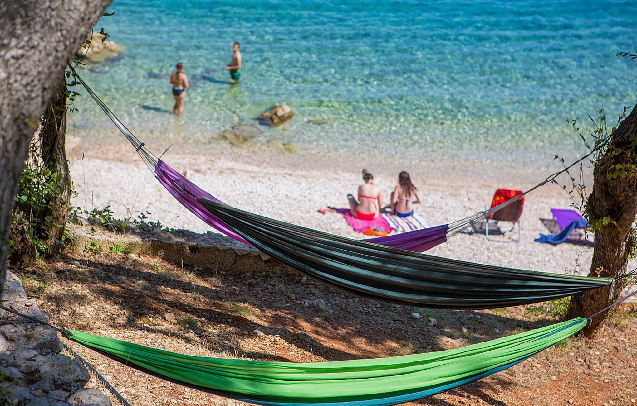Une plage avec un hamac, une eau cristalline et des personnes à l’arrière-plan.