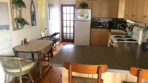 A kitchen with wooden cabinets, a refrigerator, a microwave, and a stove. There is a dining table with chairs and a window with a view. - Cozy Cottage, 1 bedroom sleeps 2 (Bradenton Beach)