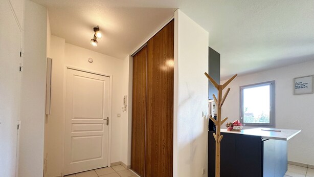 Een gang met een witte deur, een houten garderobe, een kapstok en een raam met uitzicht.