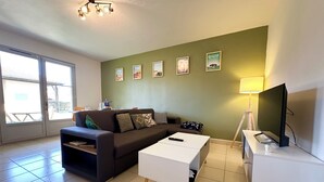 Een woonkamer met een bank, salontafel, televisie en een muur met ingelijste foto's.