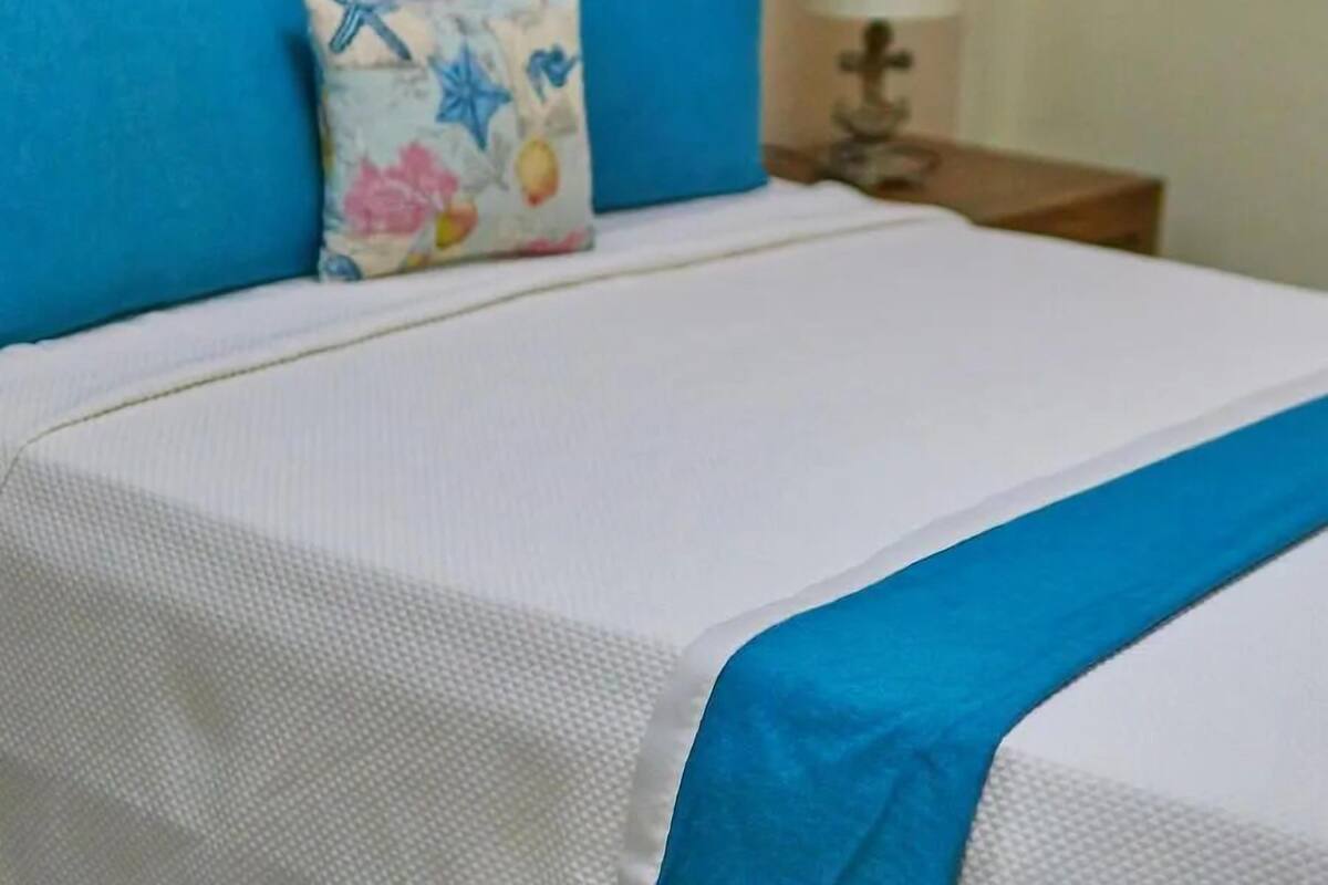 A neatly made bed with blue and white bedding, a wooden headboard, and a bedside table with a lamp.