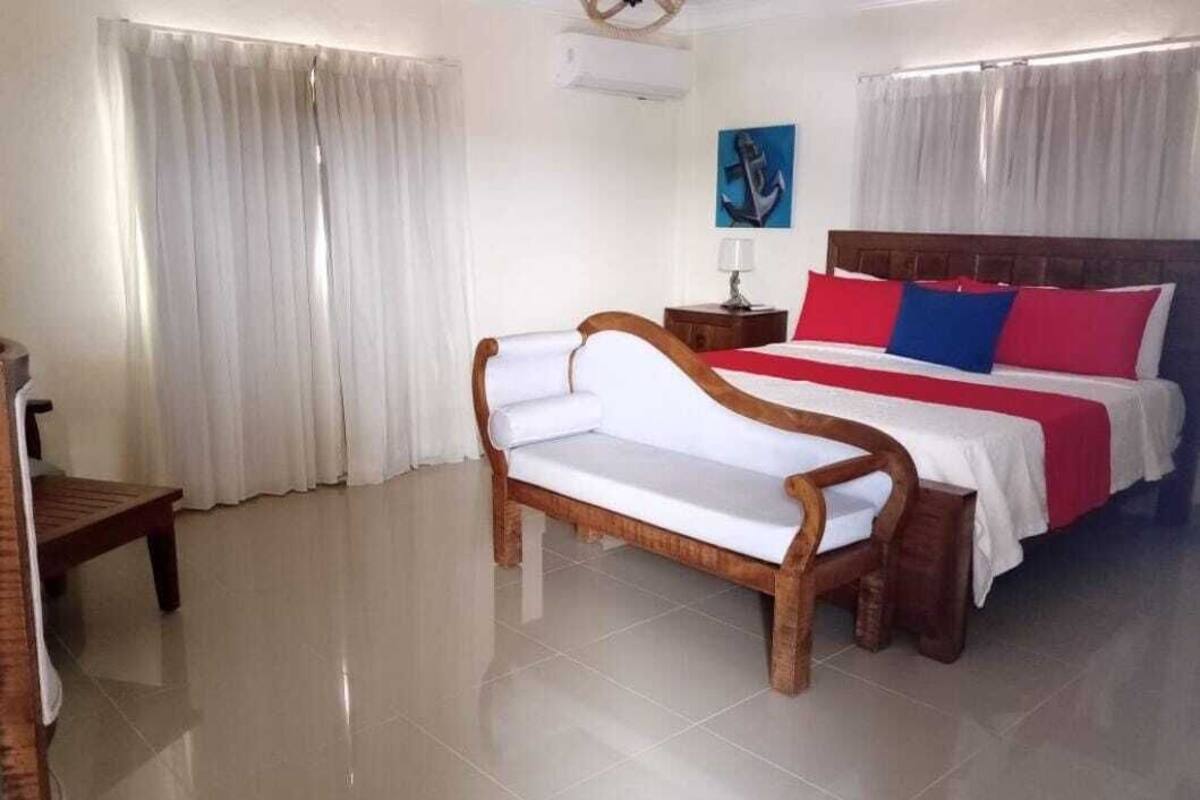 A hotel room with a bed, a wooden bench, a nightstand, and a painting on the wall.