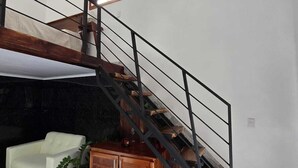 Ein modernes Wohnzimmer mit Marmorboden, einem weißen Sofa, einer Holzkommode und einer Treppe mit Metallgeländer.