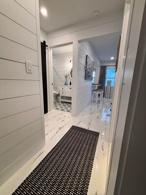 A hallway with a black and white patterned rug, a white door, and a white wall with horizontal lines.