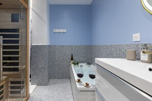 Un baño moderno con pared azul, lavamanos blanco y cabina de ducha de vidrio.