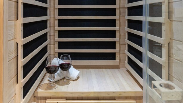 Un sauna avec des parois en bois, un banc et deux verres de vin rouge posés sur le banc.