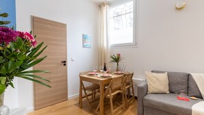 Un salon chaleureux avec un canapé gris, une table à manger en bois dressée pour deux personnes et une fenêtre agrémentée de rideaux.