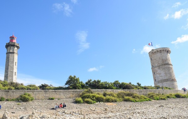 Dos torres de piedra con banderas, una playa rocosa y gente sentada en la orilla.