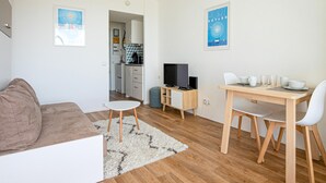 A modern, well-lit living room with a sofa, a small white table, and a TV. There is a kitchen area in the background with cabinets and a microwave. - Cozy apartment in La Rochelle with WiFi (La Rochelle)