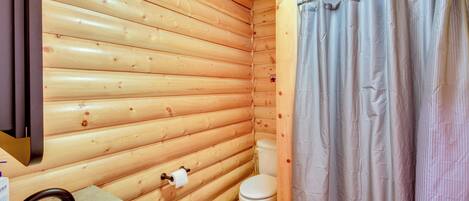 A wooden cabin bathroom with a sink, toilet, and shower curtain.