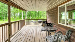Une terrasse en bois avec une rambarde, une table et des chaises, et une vue sur une forêt.