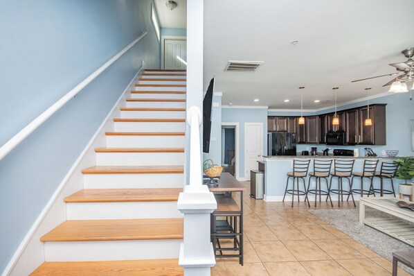 A staircase with wooden steps and white railings leading to a kitchen area with a bar and seating. - Charming 4-bedroom Myrtle Beach Home ~ Ocean View, Wi-Fi, Pool, & More! (Myrtle Beach)