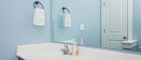 A bathroom with a white sink, dark wooden cabinets, a large mirror, and a light blue wall.