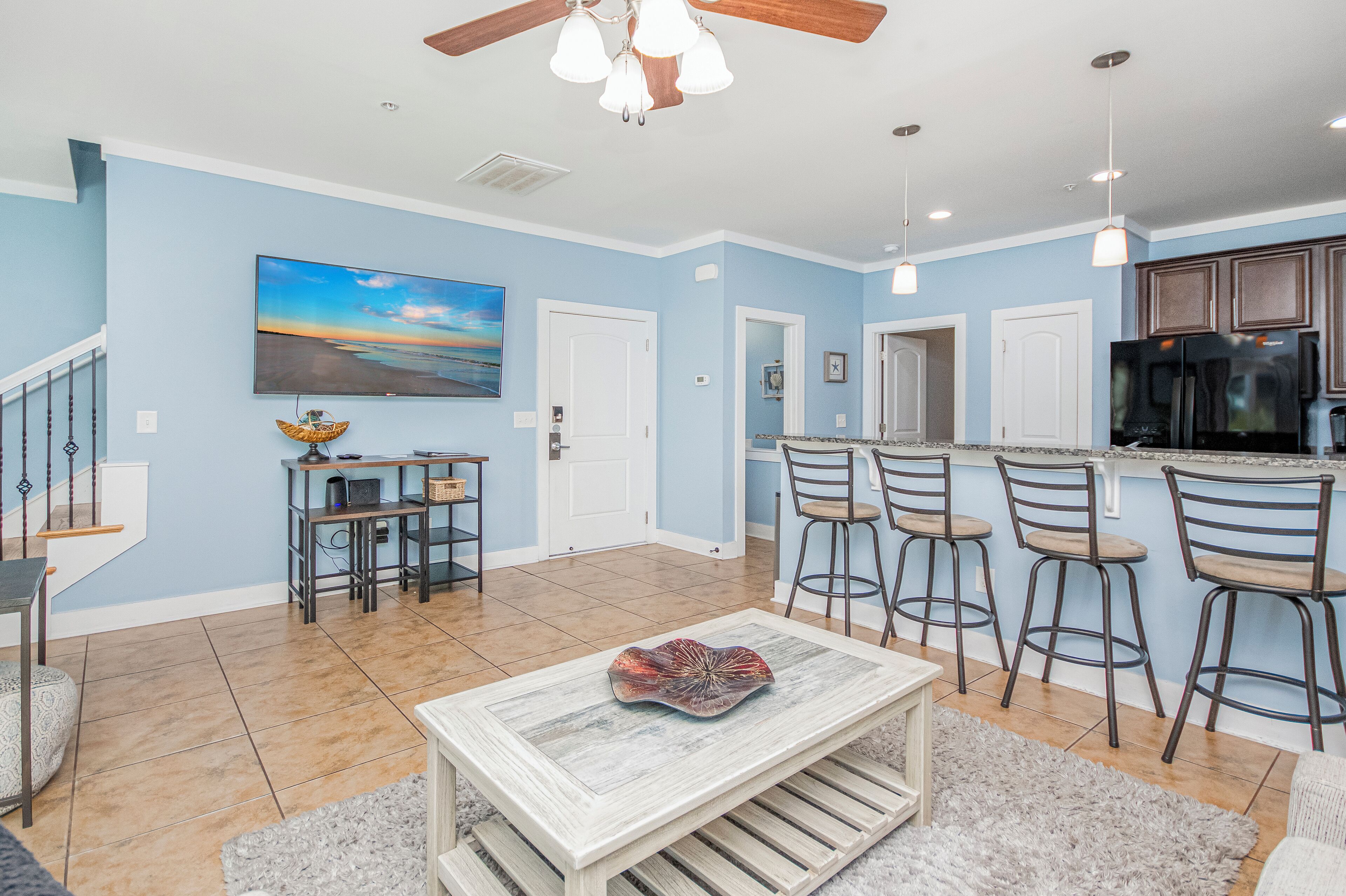 A spacious living room with a large painting, a dining area, and a kitchen with bar stools.