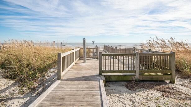A wooden boardwalk leading to a beach with a wooden fence and benches. - Charming 4-bedroom Myrtle Beach Home ~ Ocean View, Wi-Fi, Pool, & More! (Myrtle Beach)