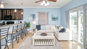 A modern kitchen with dark wooden cabinets, a bar area with stools, a white sofa, and a large window with curtains. - Charming 4-bedroom Myrtle Beach Home ~ Ocean View, Wi-Fi, Pool, & More! (Myrtle Beach)