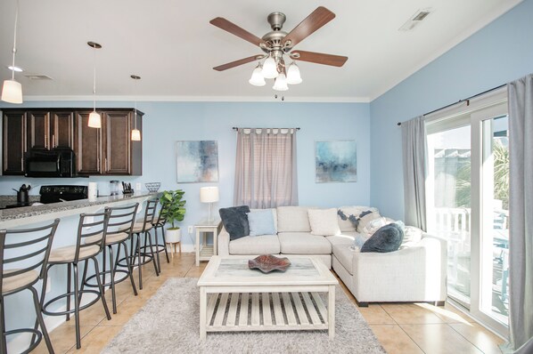 A modern kitchen with dark wooden cabinets, a bar area with stools, a white sofa, and a large window with curtains. - Charming 4-bedroom Myrtle Beach Home ~ Ocean View, Wi-Fi, Pool, & More! (Myrtle Beach)
