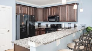 A modern kitchen with dark wooden cabinets, a black refrigerator, a microwave, and a granite countertop. There are bar stools and pendant lights above the counter. - Charming 4-bedroom Myrtle Beach Home ~ Ocean View, Wi-Fi, Pool, & More! (Myrtle Beach)