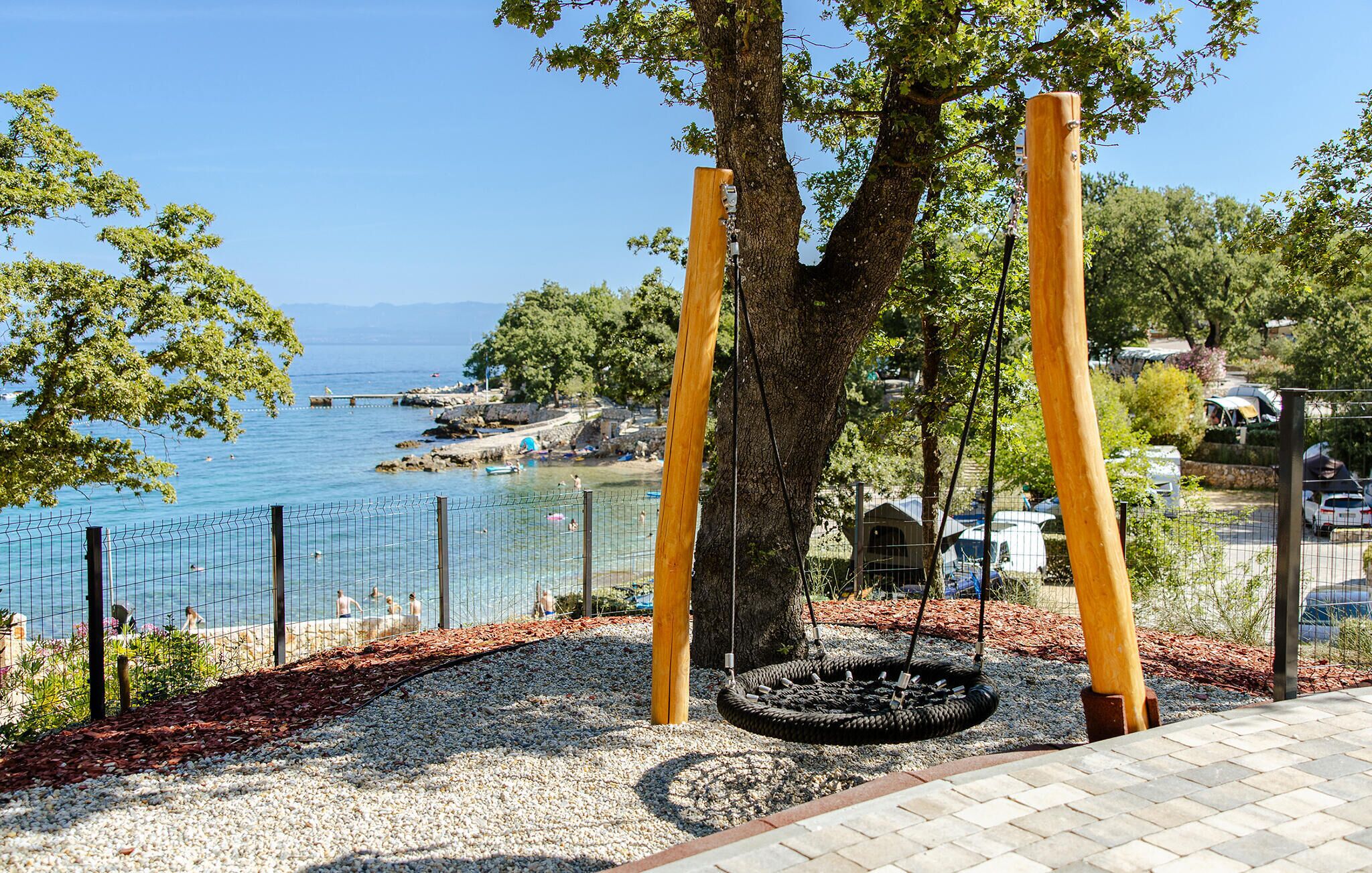 Un parc infantil amb un cadireta de pneumàtic, un arbre i vista al mar.