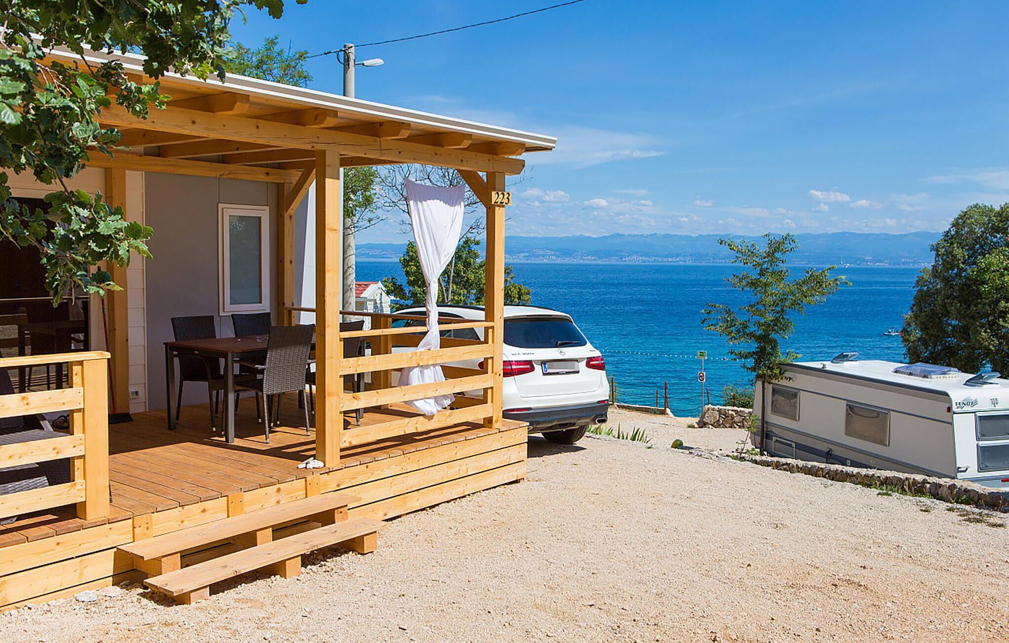 Une cabane en bois dotée d’un porche couvert, d’un coin repas et d’une voiture blanche garée devant.