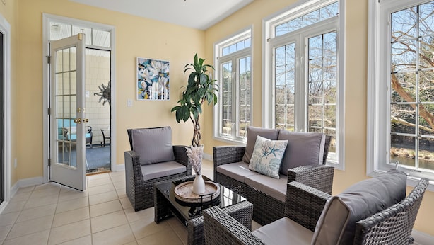 A sunlit room with wicker furniture, a glass door leading outside, and a painting on the wall.