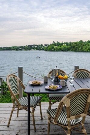 A wooden deck with wicker chairs and a table set for a meal overlooking a lake.