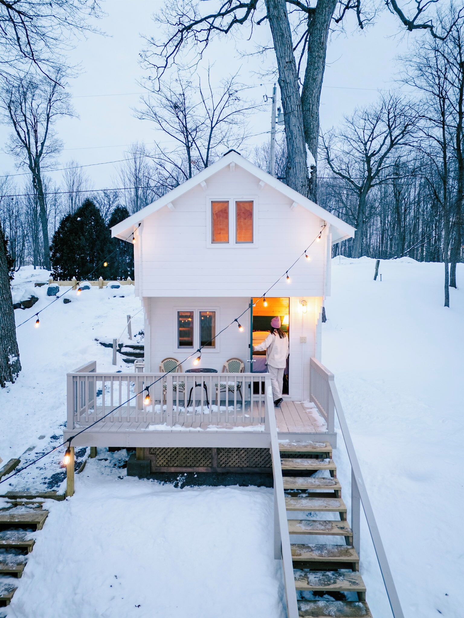 A white cabin with a deck, surrounded by snow and trees.
