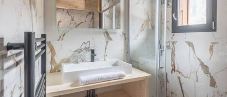 Un baño con salpicadero de mármol, tocador de madera, cabina de ducha de cristal y ventana.
