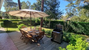 An outdoor patio with a wooden table and chairs, a barbecue grill, and a large umbrella. - CAPBRETON. Villa ALAMEAT with garden for 6 people. Free Wifi. (CAPBRETON)