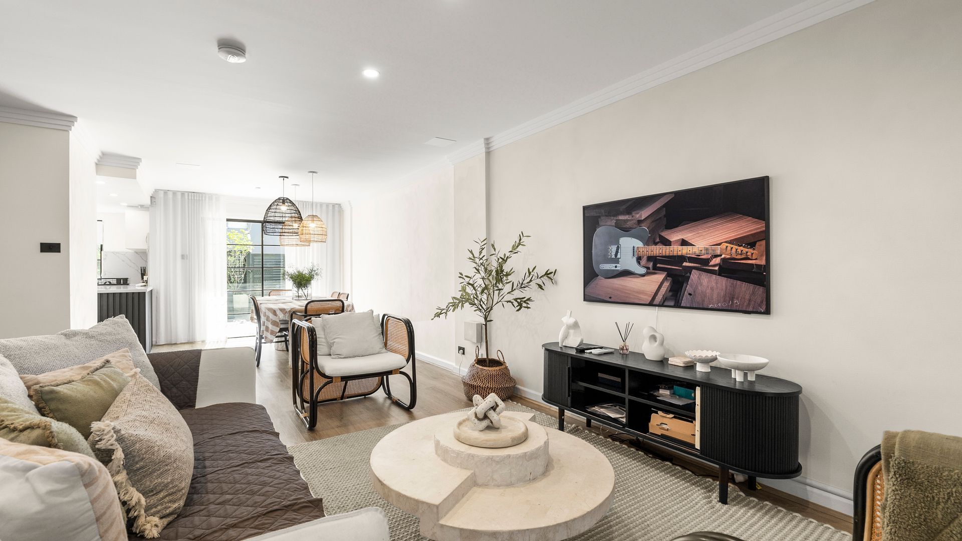 A modern living room with a sofa, a dining area with a table and chairs, a black entertainment unit, and a large framed picture on the wall.