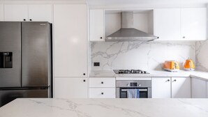 A modern kitchen with white cabinetry, a stainless steel refrigerator, a gas stove, and a built-in oven. - The Euston Social in Alexandria (Alexandria)